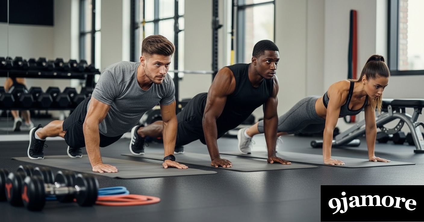 Three diverse people—two men and one woman—performing push-ups simultaneously on yoga mats in a modern gym.