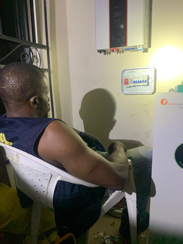 An expert solar engineer conducting a final inspection and monitoring of a Felicitysolar inverter and battery bank during a nighttime installation, delivering dependable and affordable solar energy.