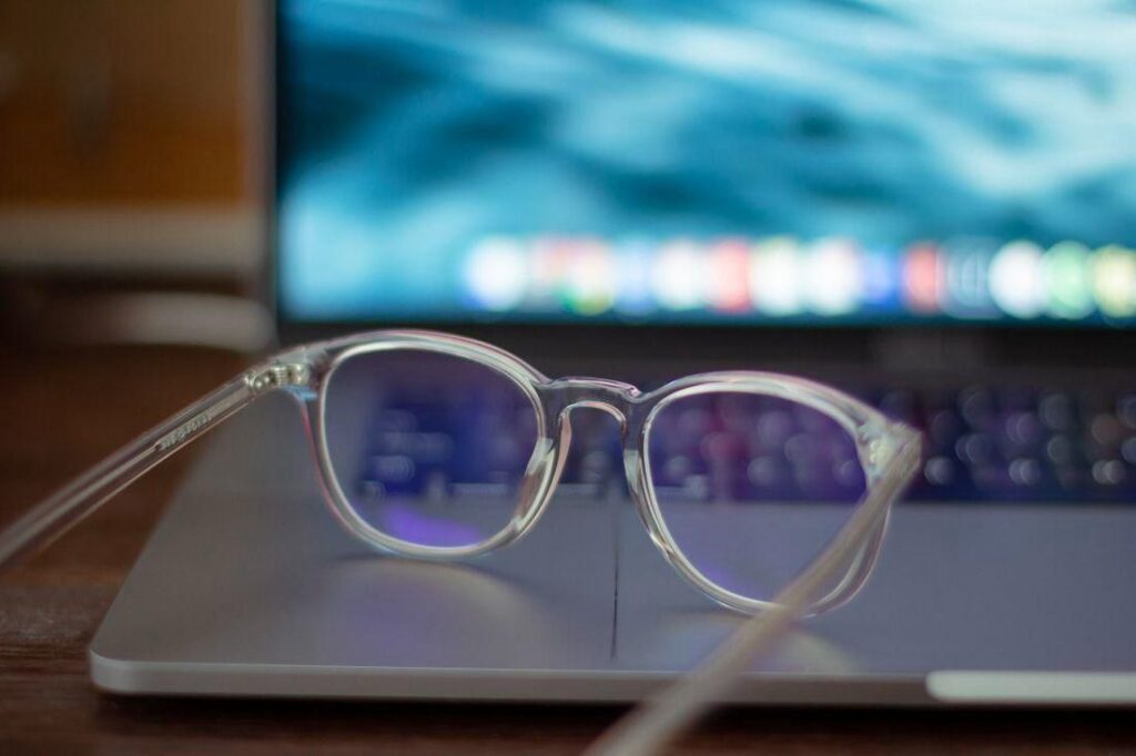Transparent round eyeglasses resting on a laptop keyboard with a blurred computer screen in the background, illustrating digital eye strain and the importance of natural ways to maintain healthy vision during prolonged screen use.
